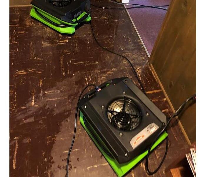 brown floors wet with water and green SERVPRO air movers on top 