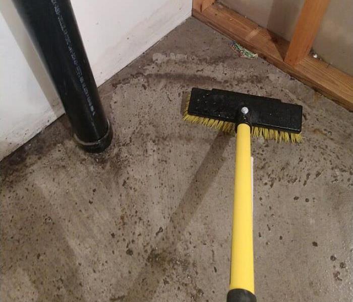 dirty floor with black and yellow push broom cleaning up the mess 