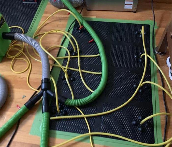 black and green mat with several cords and tubes sucking out water from a hardwood floor