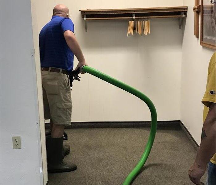 A man holding a hose extracting water from carpet. 